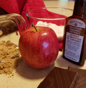 closeup of caramel extract, apple, peanut butter powder chocolate and splenda on counter next to dish towel
